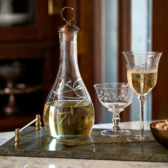 Clear glass decanter with gold cap and two wine glasses on a marble surface.