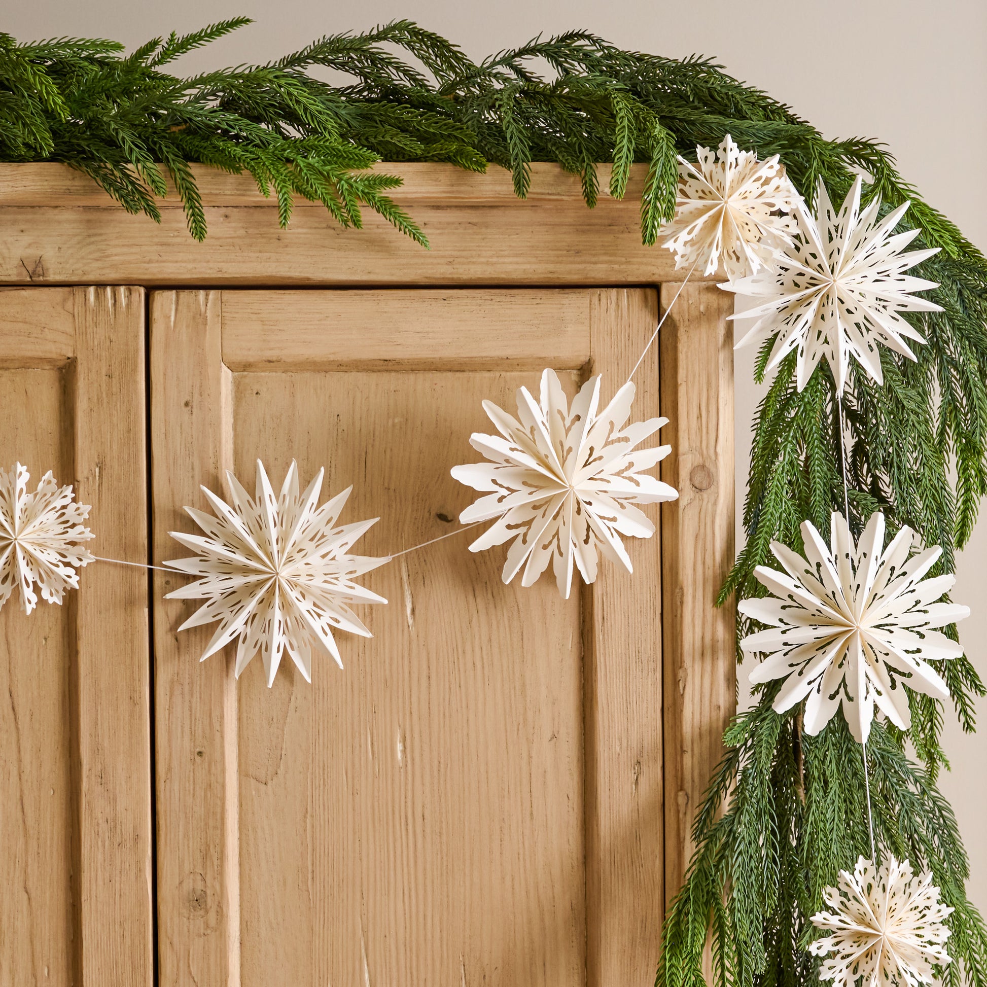Whimsical Snowflake Garland shown hung on cabinet