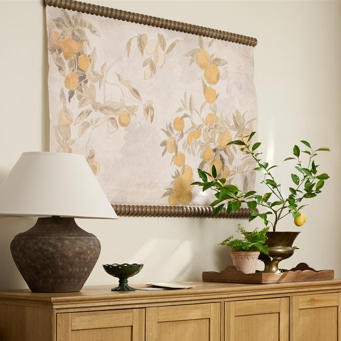 Wooden sideboard with decorative items including a lamp, bowls, and a plant, with a floral tapestry in the background.