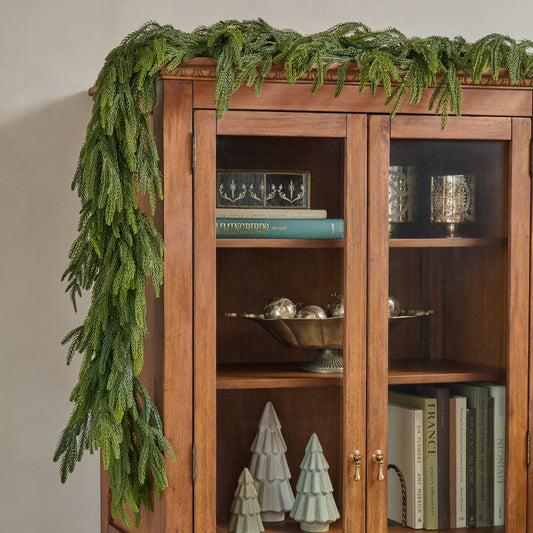Wooden cabinet with glass doors, decorative items, and a green garland on top.