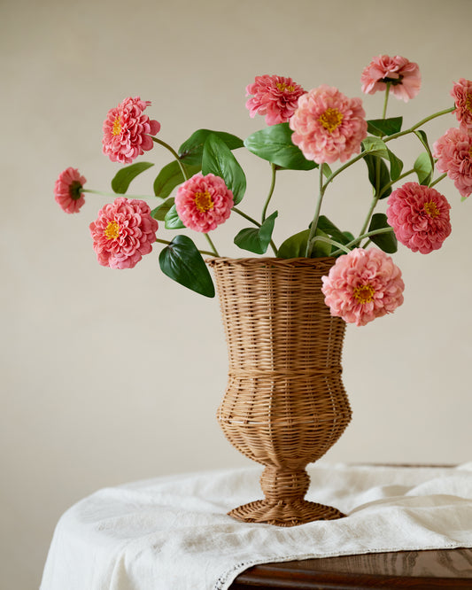 Wicker vase with pink flowers on a white surface against a beige background