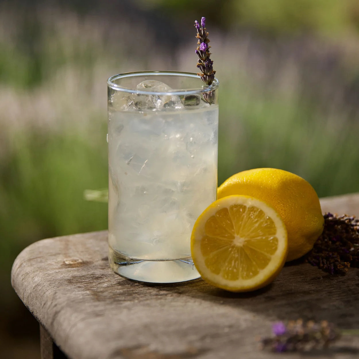 A fresh glass of lavender lemonade sitting on a wooden table outside. 