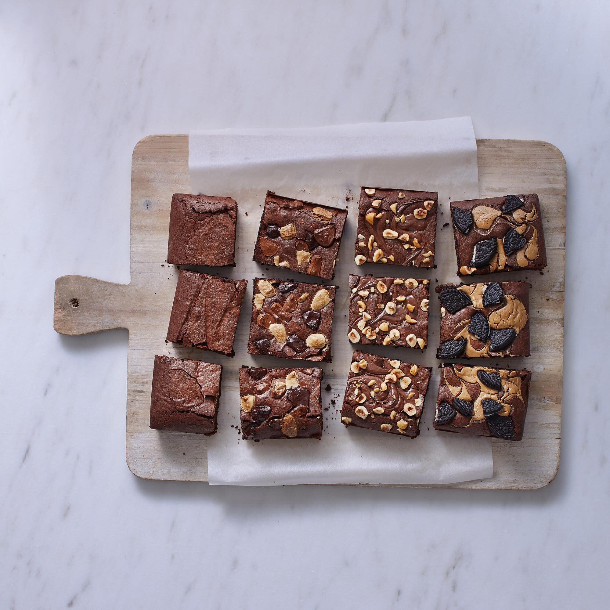 Assorted brownies on a wooden cutting board with a white marble background