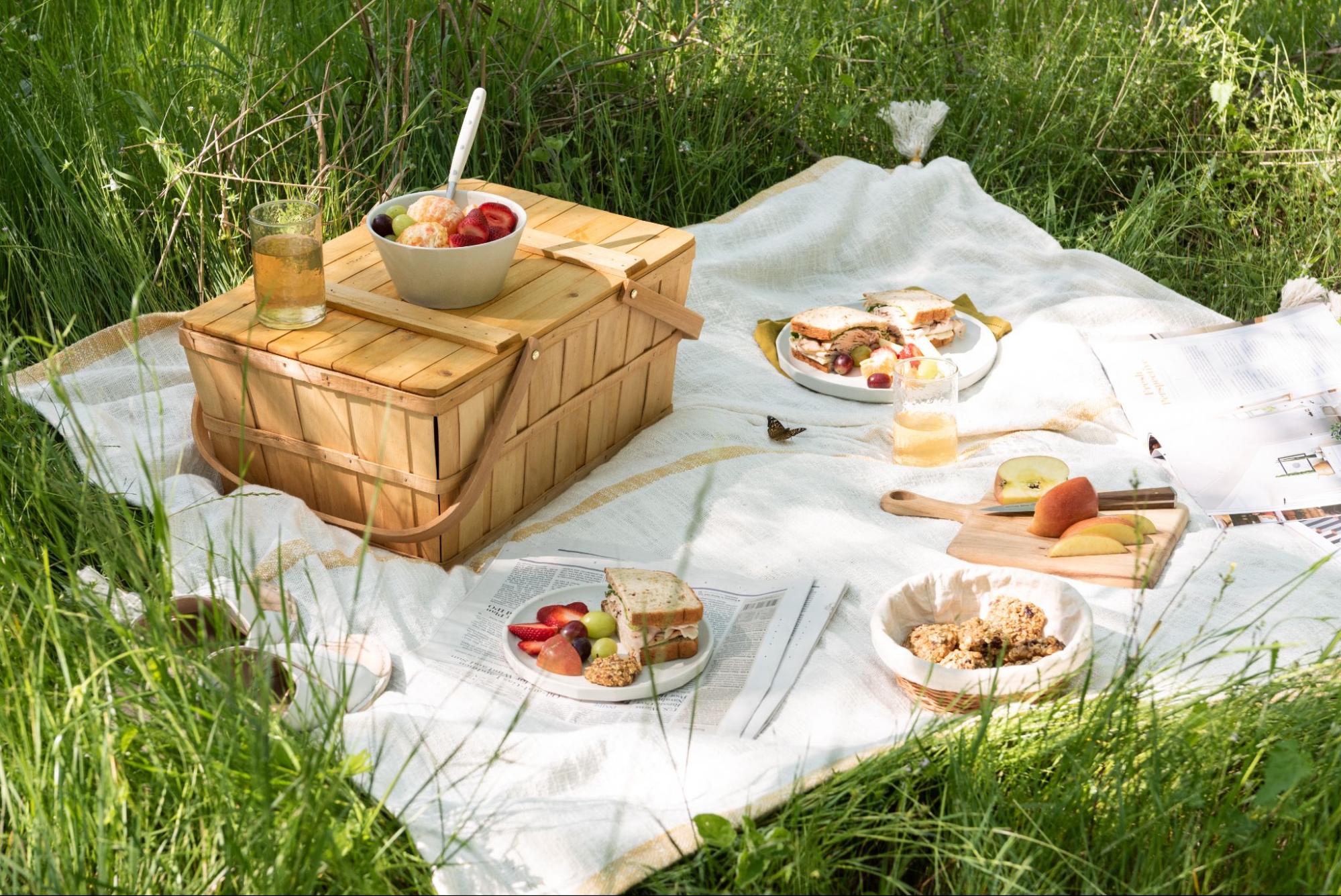 A picnic basket and snacks on a blanket. 