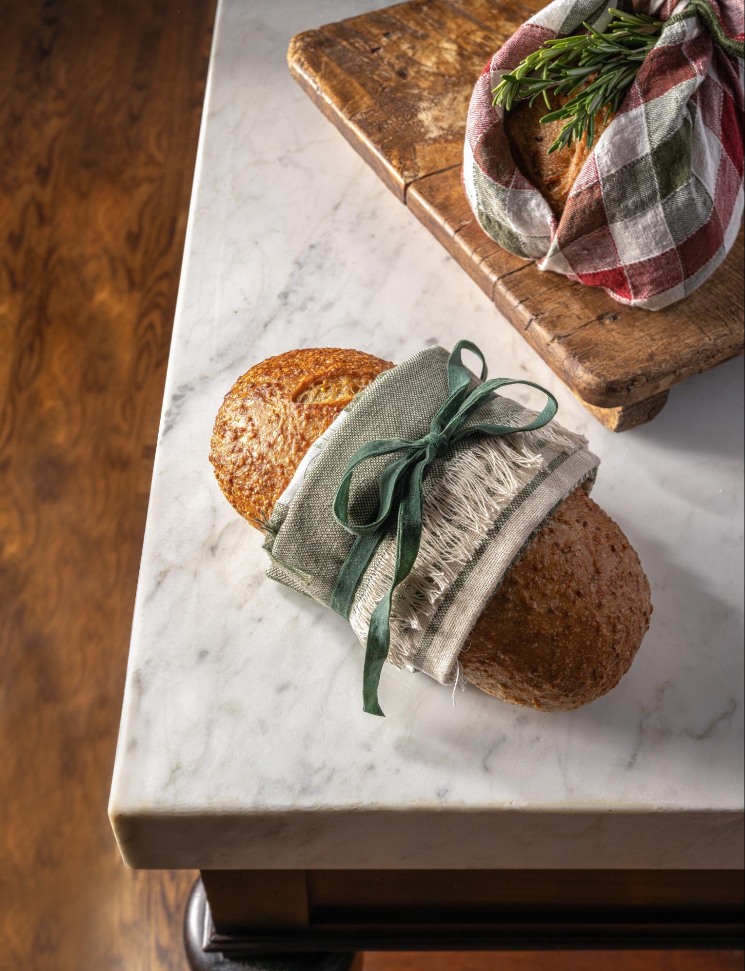 A load of bread is wrapped in a tea towel, tied with a green bow.