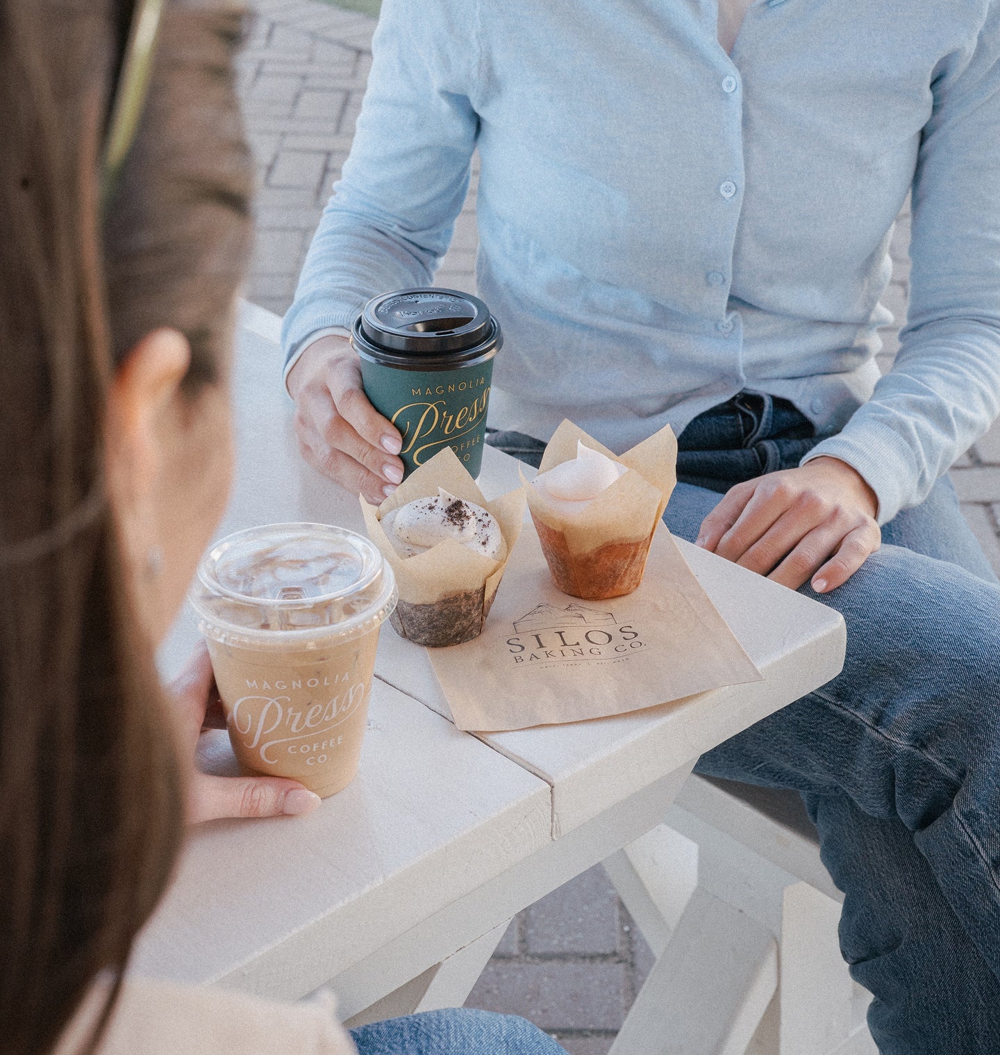 Two people sitting at a table with coffee cups and pastries, featuring 'Silos Baking Co.' and Magnolia Press Coffee branding.