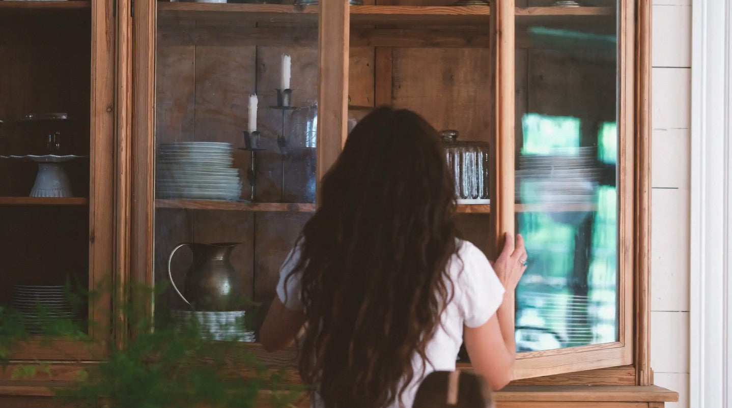 Joanna Gaines looking into a wooden cabinet with glass doors.