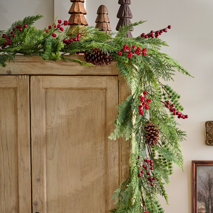 Decorative Christmas garland with greenery, red berries, and pinecones on a wooden surface.