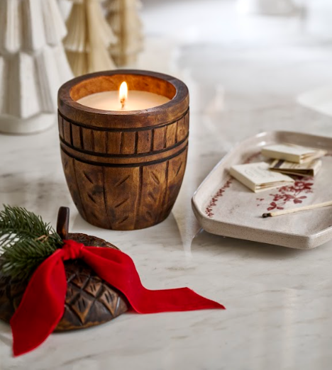 Candle in an over-sized wooden acorn on a marble surface a wooden acorn lid and red bow with pine sprig.