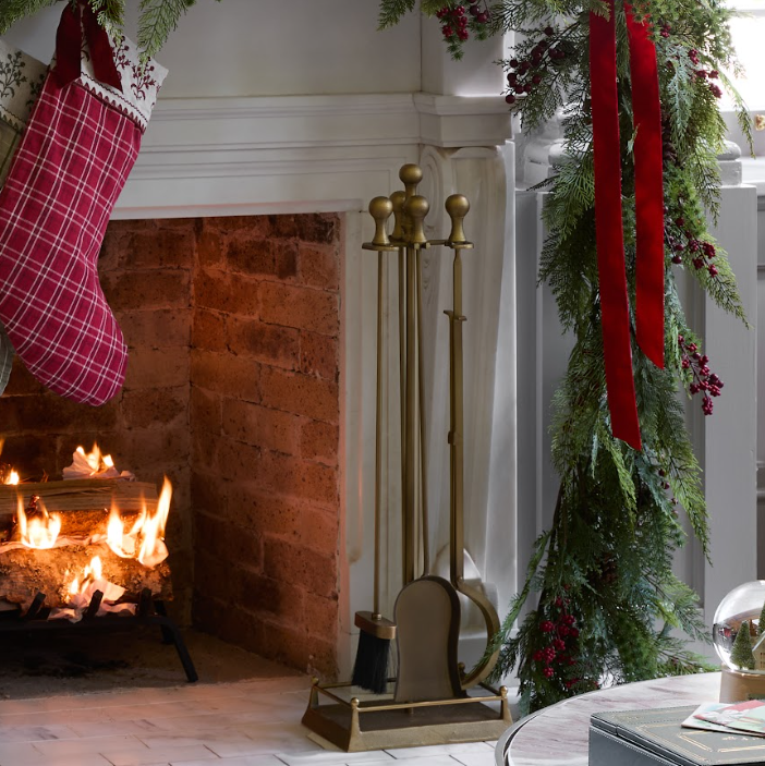 Cozy Christmas scene with a fireplace, stockings, garland and brass fireplace tools.