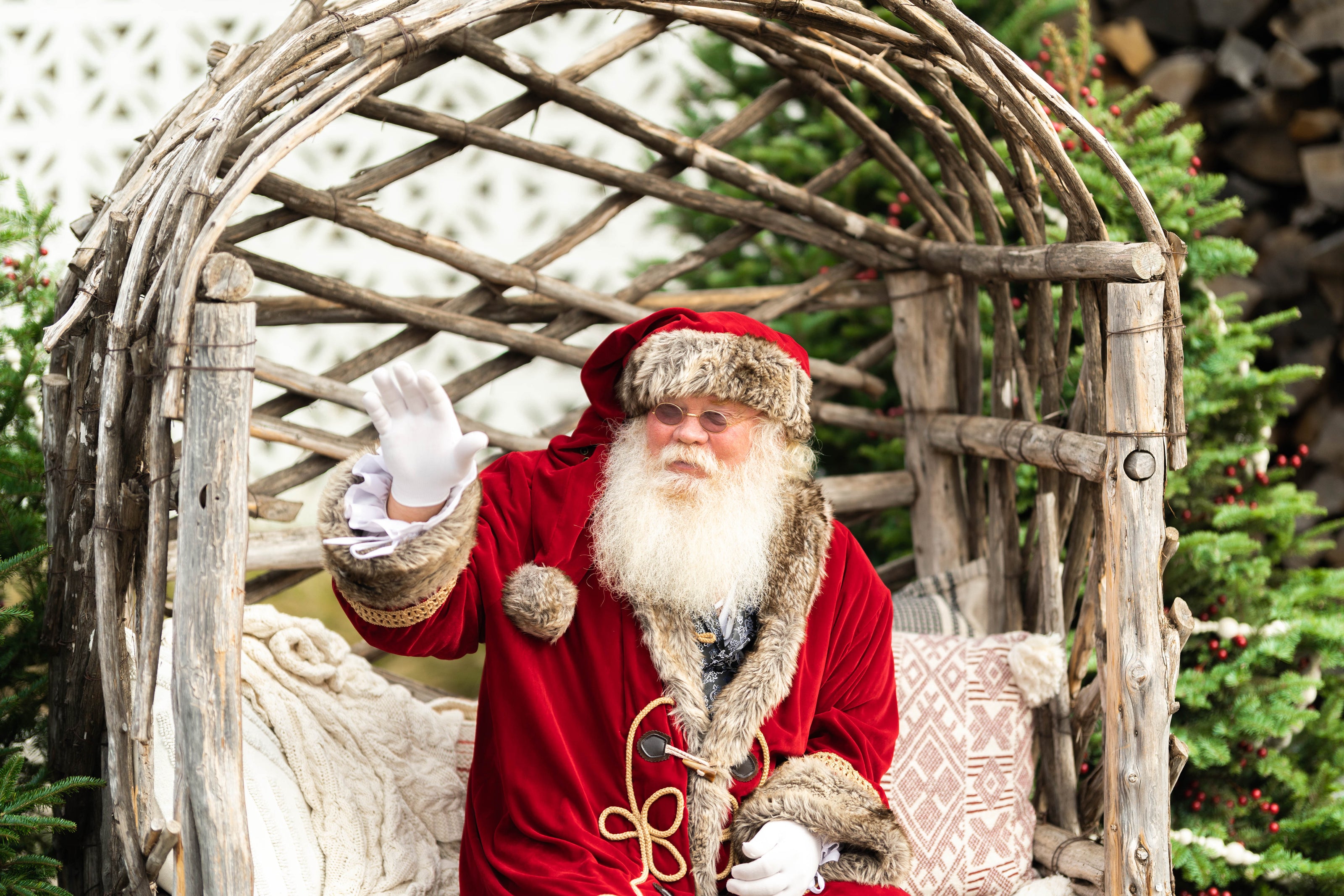 Santa Claus sitting in a decorative chair with Christmas trees in the background