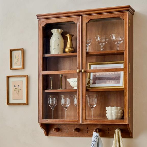 Wooden wall cabinet with glass doors displaying decorative items on a beige wall.