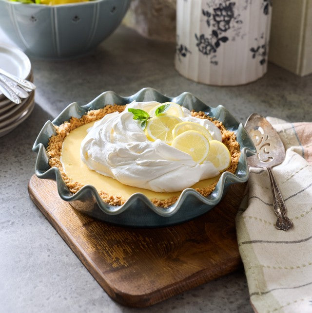 Lemon pie with whipped cream on a wooden board with a kitchen setting in the background.