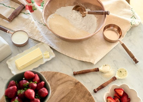 Baking ingredients and utensils on a marble countertop with a focus on flour and strawberries.