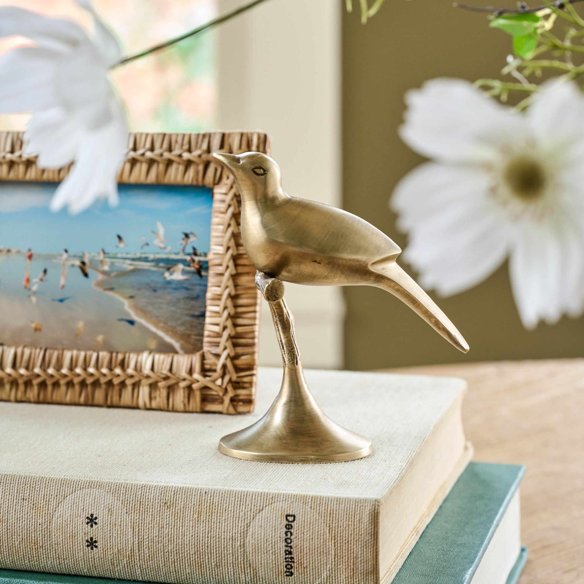 Brass bird figurine on a book with a blurred beach scene in the background
