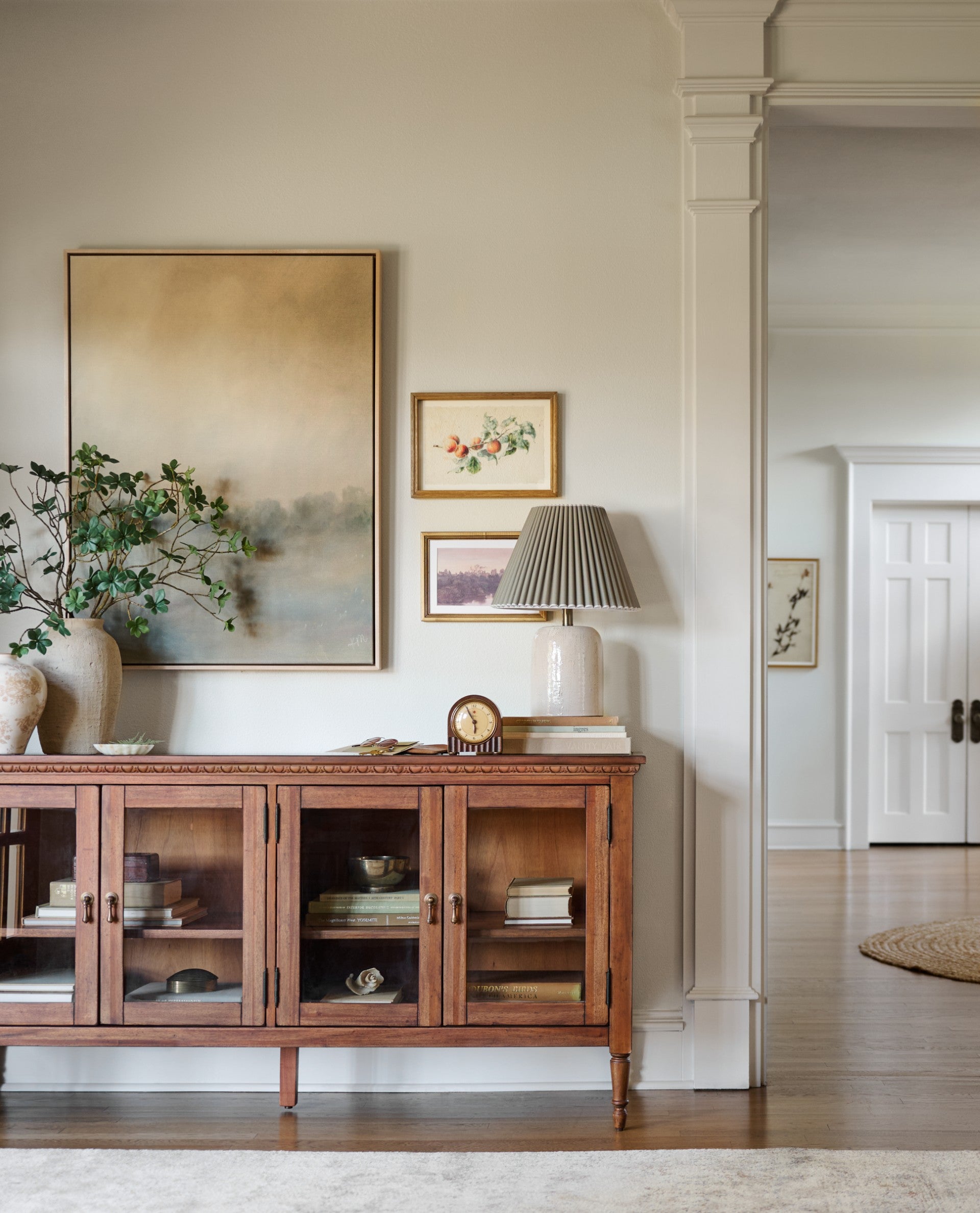 Living room with wooden sideboard, lamp, and framed pictures on a white wall.