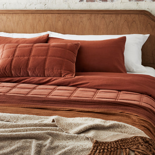 Weekend Velvet Quilt - Rustic Clay layered on a made bed with duvet covers and throw blankets