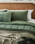 Green quilted bedding set on a bed with a wooden headboard.
