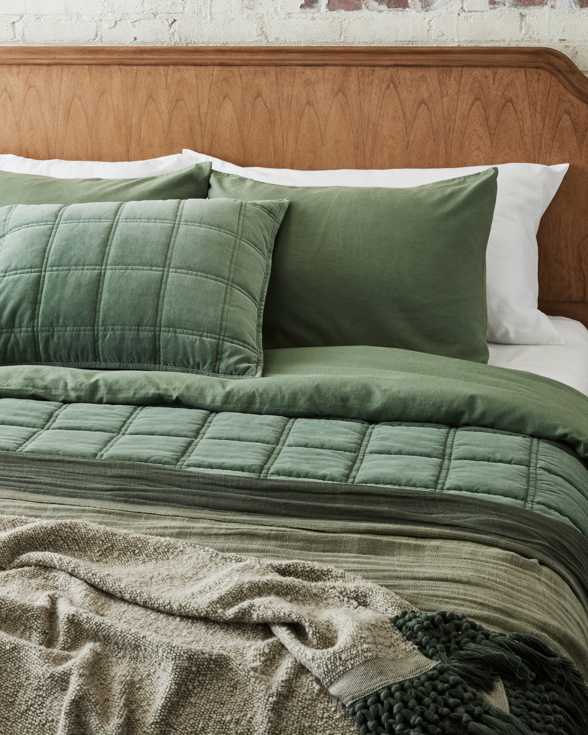Dusty Green Tassel Throw at the foot of a made bed layered with dusty green oversized throw
