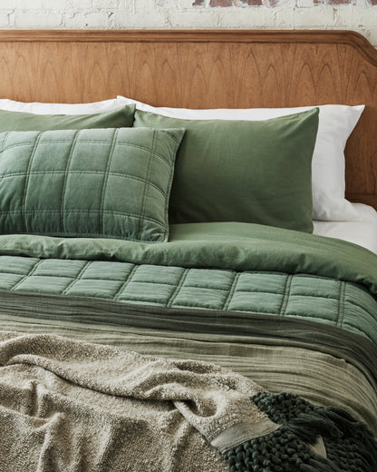 Dusty Green Tassel Throw at the foot of a made bed layered with dusty green oversized throw