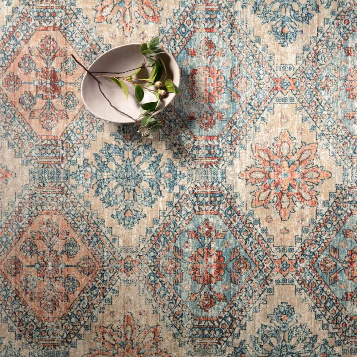 blue, orange, and tan diamond patterned rug with floral detail