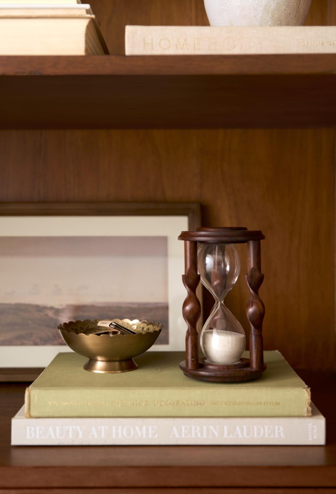 An hourglass and a small brass trinket dish sit on a stack of books.