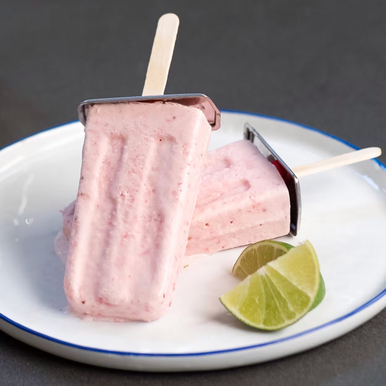 Two coconut berry pops rest on a plate with lime slices