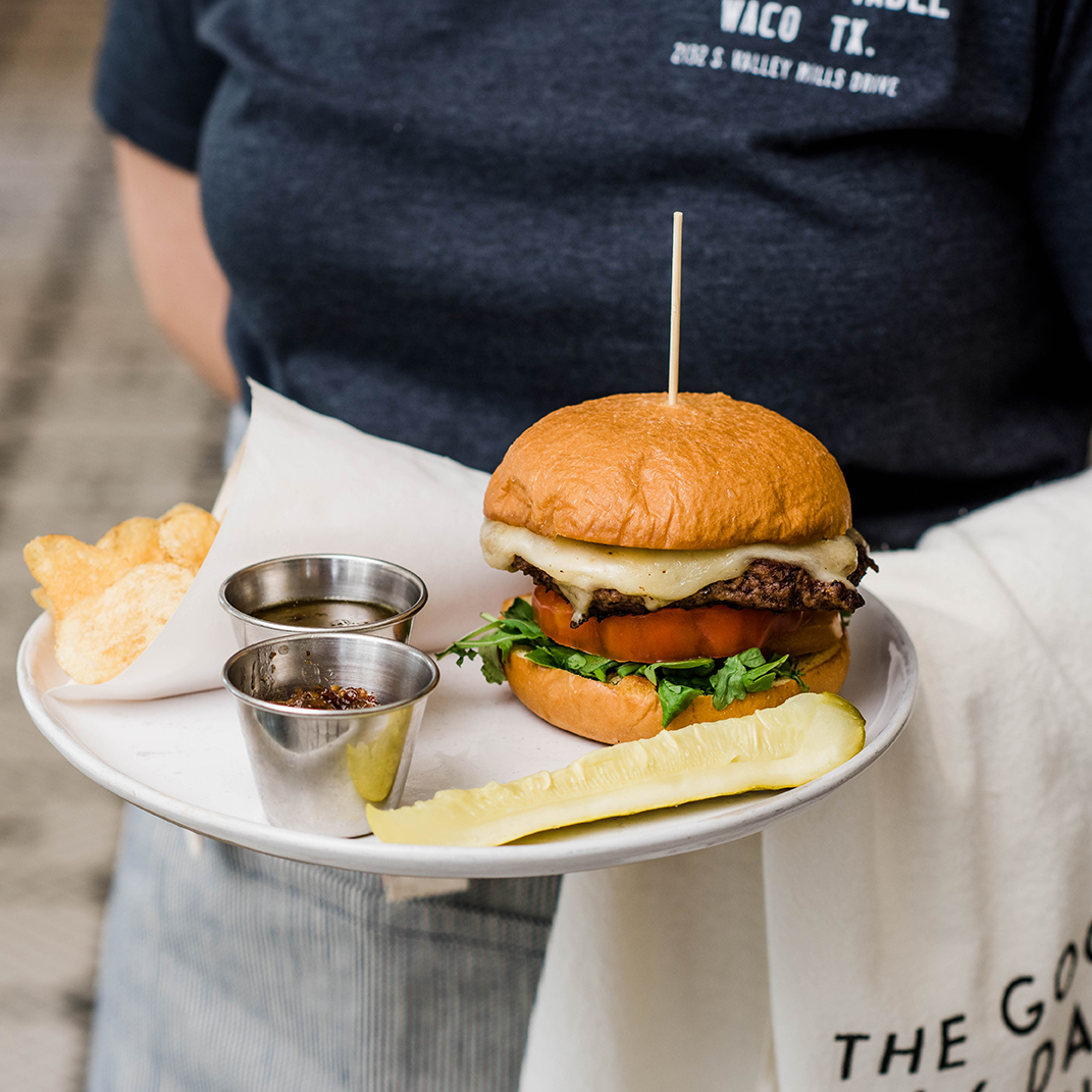 A waitress holds a tray with a hamburger and pickle on it