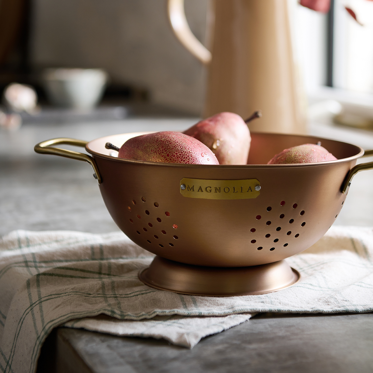 A copper colander on a counter holding pears