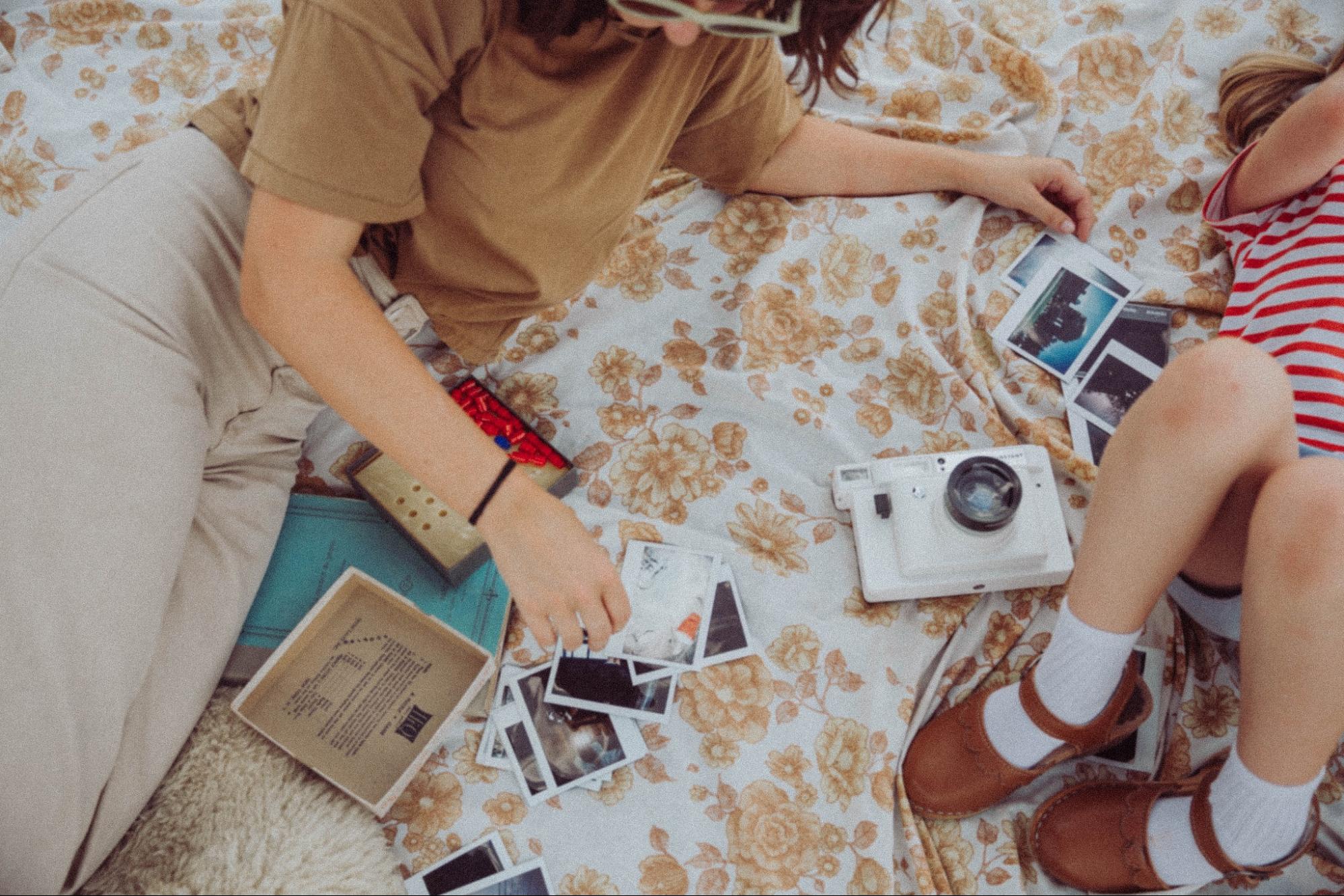 Two people spread out on a blanket with a camera and pictures, looking over the photos.
