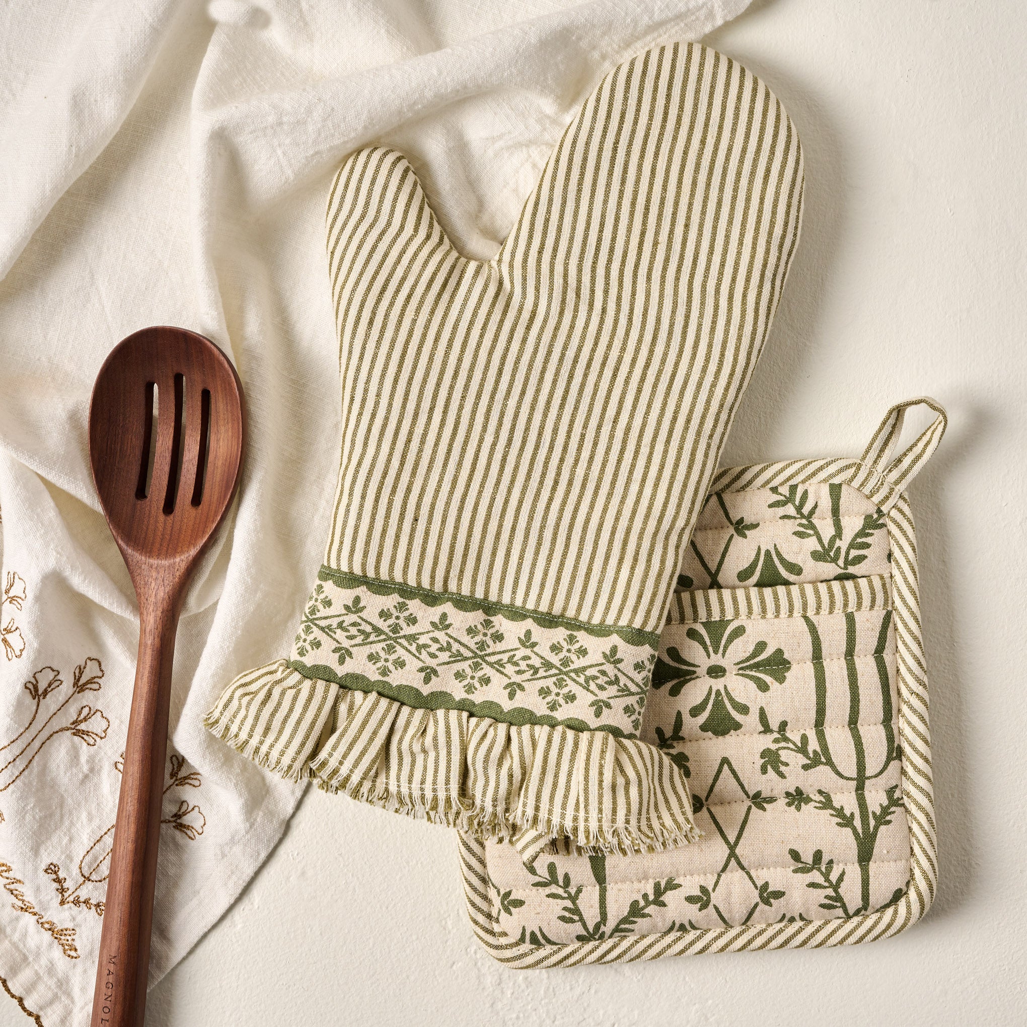 Magnolia Olive Pin Stripe Oven Mitt + Pot Holder Set shown with wooden spoon and tea towel $20.00