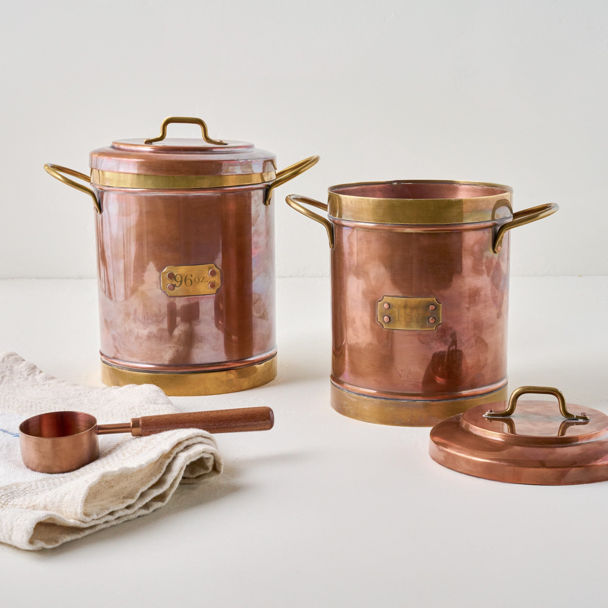 Vintage-Inspired Copper + Brass Canisters shown with measuring cup and tea towel Items range from $80.00 to $98.00