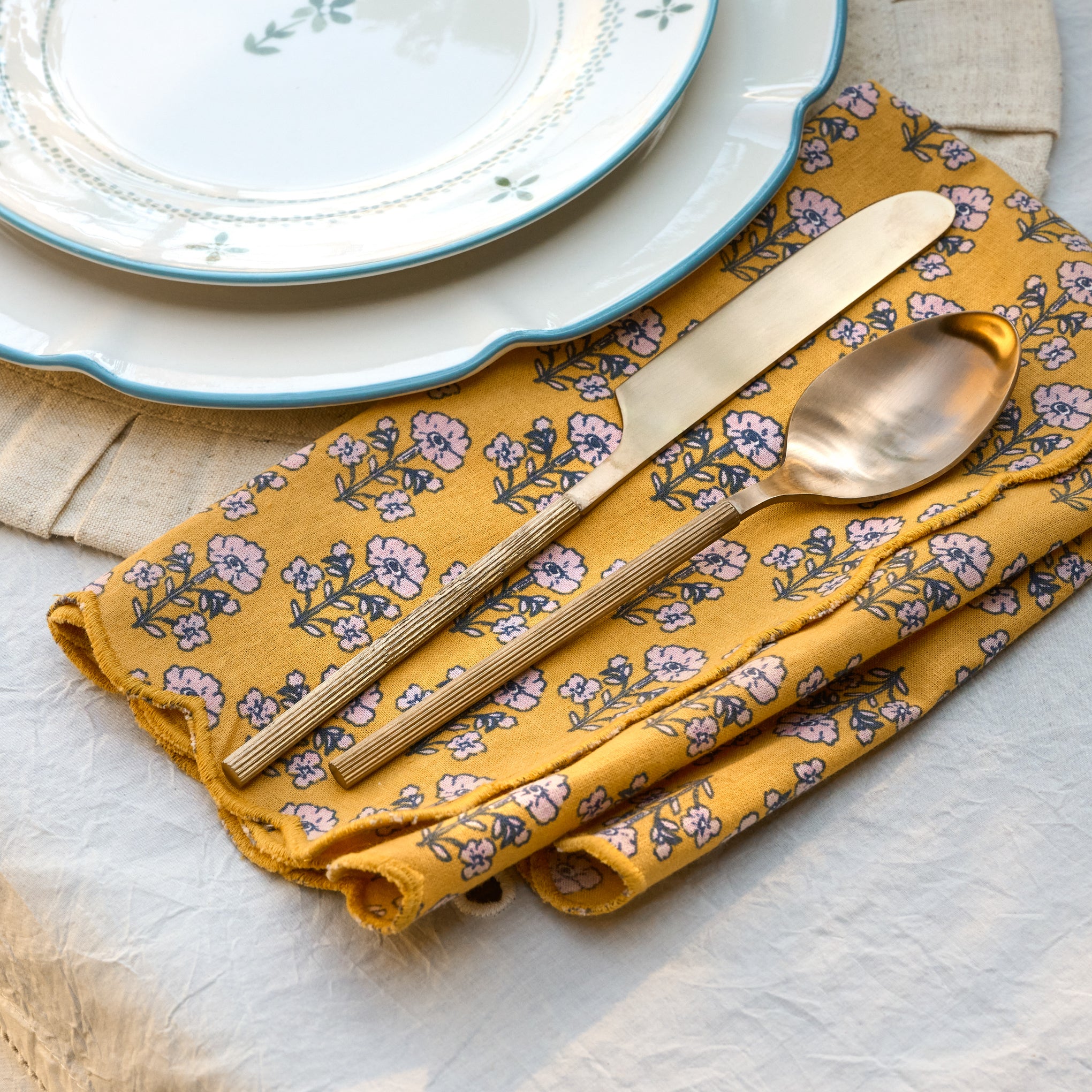 Maize Scallop Edge Block Print Napkin Set shown on table with ribbed silverware and luna plates $40.00