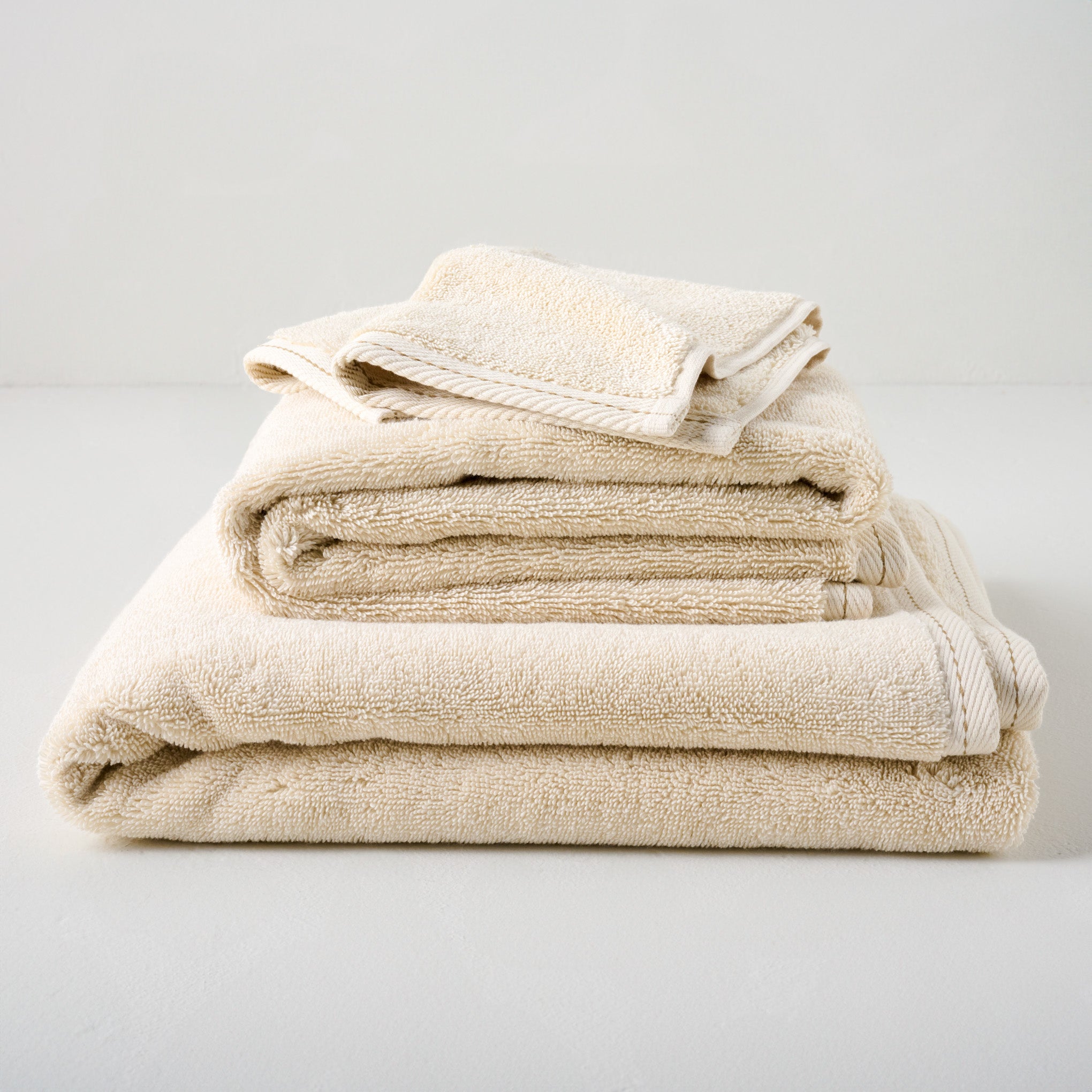 Magnolia Cream Plush Stitched Edge Towels shown stacked Items range from $14.00 to $42.00