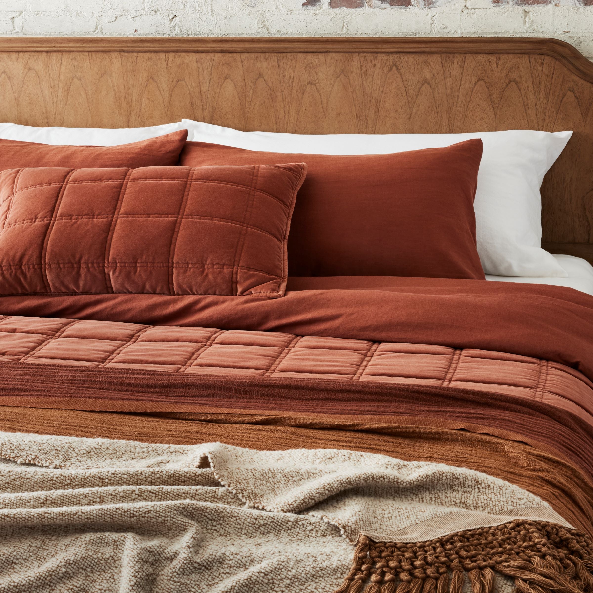 Weekend Velvet Quilt - Rustic Clay layered on a made bed with duvet covers and throw blankets